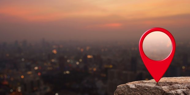 Red location icon on a rock overlooking a city at dusk