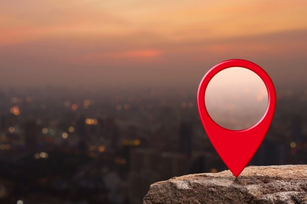 A location marker on a cliff overlooking a city at dusk